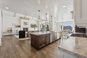 Kitchen featuring a fireplace, dark brown cabinetry, light stone counters, open floor plan, and pendant lighting