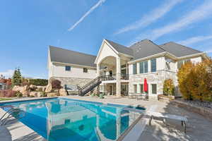 Back of property with stone siding, stairway, a patio, an outdoor pool, and roof with shingles