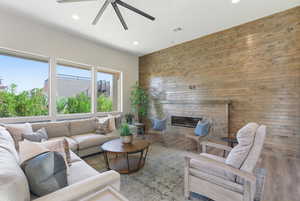 Living room featuring a glass covered fireplace, a ceiling fan, wood finished floors, recessed lighting, and wooden walls