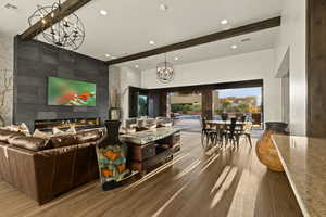 Living room with a fireplace, an accent wall, wood finished floors, recessed lighting, and beamed ceiling