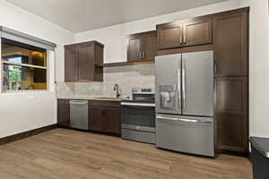 Kitchen featuring dark brown cabinets, stainless steel appliances, backsplash, and wood tiled floors