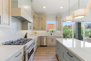 Kitchen featuring appliances with stainless steel finishes, premium range hood, backsplash, light stone countertops, and light wood-style floors