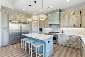 Kitchen featuring light stone countertops, high end appliances, hanging light fixtures, a kitchen bar, and a center island