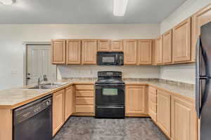 Kitchen with black appliances, light countertops, light brown cabinetry, and a peninsula