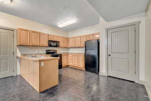 Kitchen featuring light countertops, black appliances, light brown cabinetry, dark tile patterned floors, and a peninsula