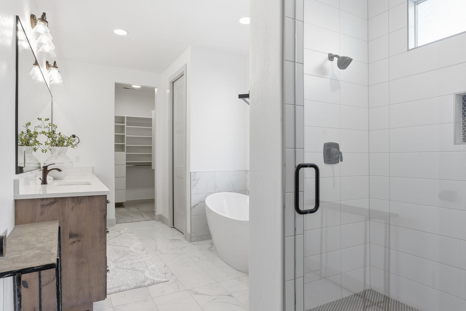 Full bath with a spacious closet, a freestanding tub, double vanity, light marble finish floors, and a stall shower