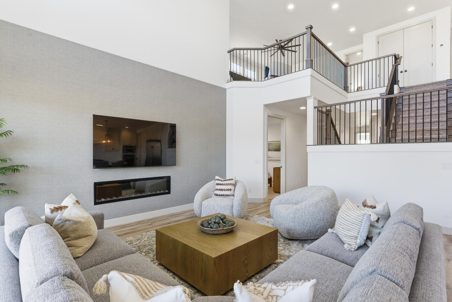 Living area featuring a towering ceiling, wood finished floors, a glass covered fireplace, recessed lighting, and stairway