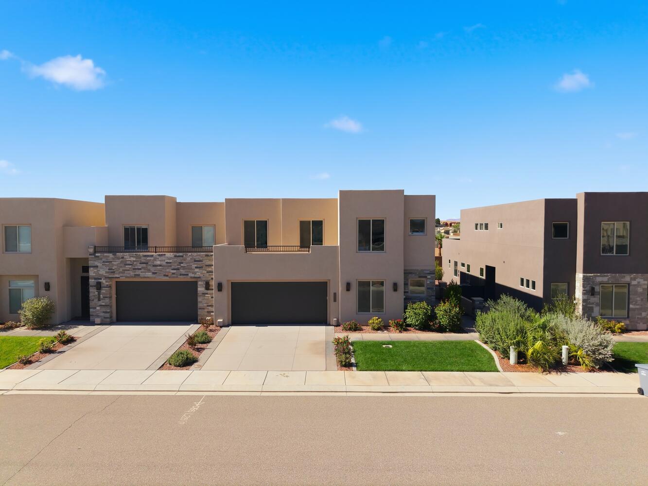 Pueblo revival-style home with stucco siding, driveway, a garage, and stone siding