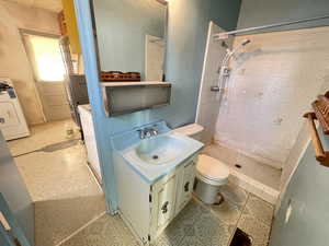 Bathroom featuring vanity, washer and clothes dryer, a tile shower, and light flooring