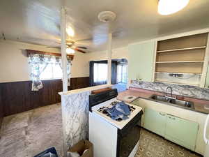 Kitchen with wooden walls, a wainscoted wall, white gas range, green cabinetry, and open shelves