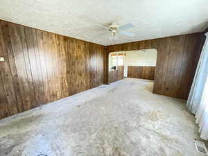 Spare room featuring arched walkways, ceiling fan, carpet flooring, a textured ceiling, and wood walls