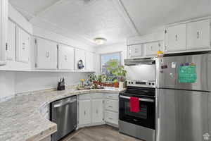 Kitchen featuring appliances with stainless steel finishes, white cabinets, light countertops, a textured ceiling, and light wood-style floors