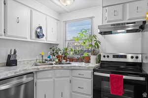 Kitchen with stainless steel appliances, white cabinetry, under cabinet range hood, and light stone countertops