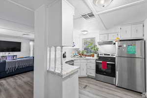 Kitchen with appliances with stainless steel finishes, white cabinetry, light wood-type flooring, under cabinet range hood, and open floor plan