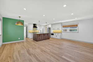 Kitchen with white cabinetry, hanging light fixtures, open floor plan, recessed lighting, and an island with sink