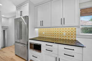 Kitchen with appliances with stainless steel finishes, tasteful backsplash, white cabinets, light wood-style flooring, and dark stone countertops
