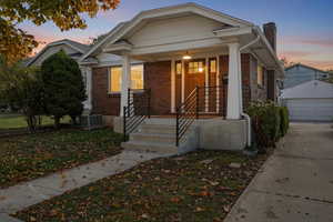 Bungalow with a porch, brick siding, a chimney, a detached garage, and an outbuilding