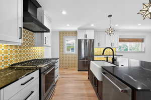 Kitchen featuring appliances with stainless steel finishes, tasteful backsplash, wall chimney exhaust hood, white cabinetry, and recessed lighting