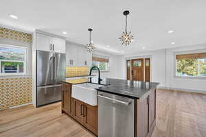 Kitchen with appliances with stainless steel finishes, brown cabinetry, decorative light fixtures, a kitchen island with sink, and light wood-style floors