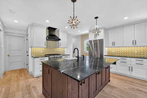 Kitchen featuring white cabinets, a center island with sink, dark stone countertops, premium appliances, and dark brown cabinets