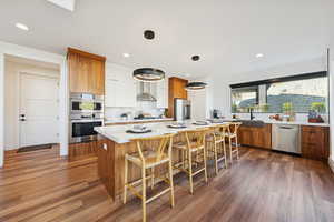 Kitchen featuring modern wood cabinets, island, hanging light fixtures, backsplash, and stainless steel appliances