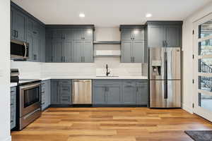Basement apartment kitchen with stainless steel appliances, light wood-style floors, recessed lighting, and gray cabinetry