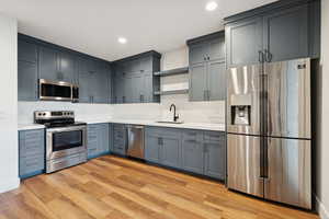 Basement apartment kitchen with stainless steel appliances, light wood-style floors, recessed lighting, and gray cabinetry