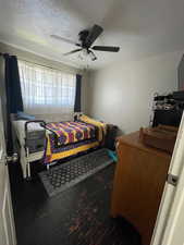 Bedroom with a textured ceiling, dark wood finished floors, and a ceiling fan