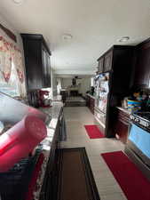 Kitchen featuring stainless steel gas range, a textured ceiling, open floor plan, dark brown cabinetry, and light stone counters