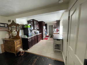 Kitchen with wood finish floors, dark brown cabinets, a textured ceiling, light stone countertops, and stainless steel refrigerator with ice dispenser