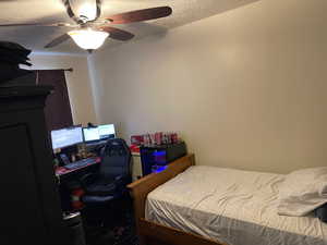 Bedroom with ceiling fan, a textured ceiling, and a desk