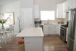 Kitchen with appliances with stainless steel finishes, white cabinets, a center island, light stone countertops, and dark wood-type flooring
