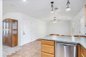 Kitchen featuring stainless steel dishwasher, a peninsula, light tile patterned floors, vaulted ceiling, and hanging light fixtures