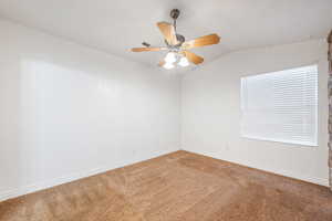 Carpeted empty room featuring vaulted ceiling and a ceiling fan