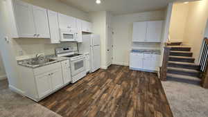 Kitchen featuring white appliances, white cabinetry, light countertops, recessed lighting, and dark wood finished floors