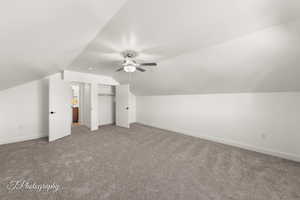 Additional living space featuring lofted ceiling, dark colored carpet, and a ceiling fan