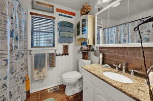 Full bath featuring vanity, a shower with shower curtain, dark tile patterned flooring, wood walls, and decorative backsplash