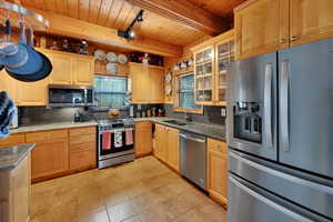 Kitchen with appliances with stainless steel finishes, tasteful backsplash, a wood ceiling with exposed beams, dark stone counters, and glass insert cabinets