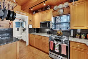 Kitchen with decorative backsplash, stainless steel appliances, light stone countertops, a wood ceiling with exposed beams, and light tile patterned floors