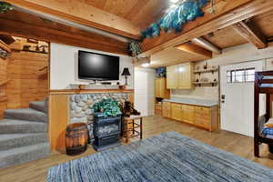Living area featuring a wood stove, wooden walls, light wood-style floors, a wood ceiling with exposed beams, and stairway