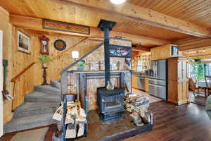 Living area featuring a wood stove, a wood ceiling with exposed beams, wood walls, dark wood-type flooring, and stairway