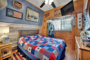 Bedroom featuring wooden walls, hardwood / wood-style floors, a ceiling fan, and a wainscoted wall