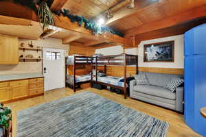 Bedroom with wood walls, light wood-type flooring, a wood ceiling with exposed beams, and track lighting
