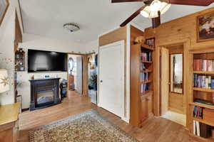 Living room featuring light wood-style flooring, wood walls, and ceiling fan