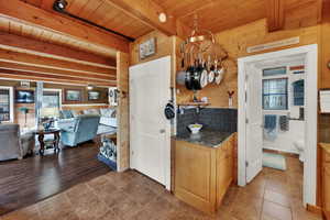 Kitchen with dark stone countertops, a wooden ceiling with exposed beams, wooden walls, decorative backsplash, and light tile patterned floors