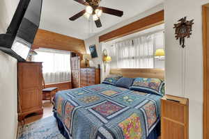 Bedroom featuring ceiling fan, wood finished floors, and wooden walls