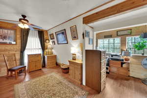 Office space featuring wood walls, light wood-style floors, plenty of natural light, crown molding, and a ceiling fan