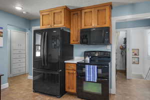 Kitchen with black appliances, brown cabinetry, light countertops, and a textured ceiling