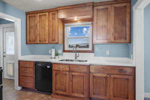 Kitchen featuring brown cabinetry, black dishwasher, light countertops, and a textured ceiling