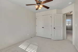 Unfurnished bedroom featuring light colored carpet, a ceiling fan, and a closet